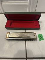 M. Hohner harmonica displayed with its green and red protective hard case.