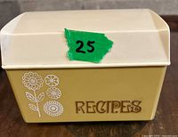 Closed view of vintage pale yellow and cream Lustro Ware recipe box with floral design and 'RECIPES' label on front