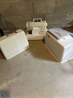 Singer sewing machine with carrying case on a concrete surface.