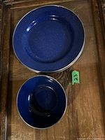 Stack of 4 blue enamel plates and 4 blue enamel bowls with white speckled pattern and silver rims seen from above