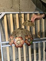 Full view of the Capiz shell lamp hanging by metal chain with a hand holding the top cap showing scale and detail.