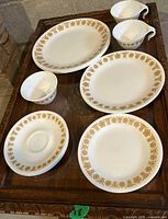 Photo showing four oval plates, two teacups, saucer, and sauce cup all with gold butterfly design on white Corelle glass.