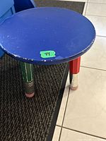 Close-up photo of blue round stool top with paint chipping and green sticker.