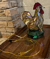 View of the rooster stained glass lamp showing the front and side detailing with yellow electric cord visible.