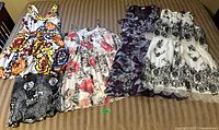 Five women's summer dresses and one skirt laid out on a striped cushioned surface, showing floral patterns and varied designs.