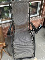 Front view of zero gravity lounge chair showing worn gray mesh and black frame with armrests