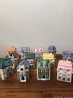 All 12 ceramic village spice jars arranged in three rows on wooden surface against plain wall