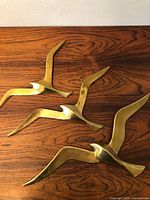Three gold-toned brass birds on wooden surface, showing overall look of items and scale.