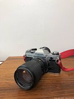 Canon AE-1 camera angled showing front and side with attached lens and red strap