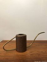 Front side view of a vintage mid century modern copper and brass watering can showing textured copper body and curved brass spout and handle.