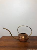 Side view of the mid century modern copper and brass watering can showing the hammered copper body and curved brass handle and spout.