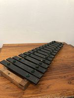 Metal Glockenspiel with black metal bars mounted on a natural wood base, bars labeled with musical notes, arranged on a flat surface.