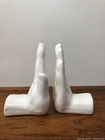 Side view of two white ceramic hands bookends positioned facing each other upright on a wooden surface