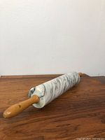 Full view of the marble rolling pin featuring wooden handles on both ends and natural gray veining on the marble surface.
