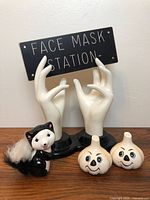 View of all lot items together: two ceramic hands with sign, skunk figurine, and two garlic bulb decorations