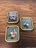 Three small framed miniature flower paintings laid out on wooden surface