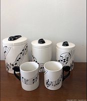 Full set of three ceramic canisters with lids and two mugs, all with musical notes design