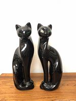 Pair of vintage black ceramic cat figurines sitting upright on a white background, showing full bodies