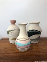Front view of three hand painted clay pottery vases with southwestern style designs on a wooden surface against a white wall.