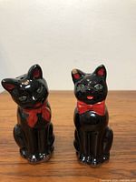 Front view of both black cat salt and pepper shakers showing the front detail, including red bows and painted eyes.