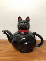 Front view of black cat teapot with red bow tie and spout visible.