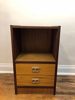 Front view of the Mid Century Modern teak nightstand showing two drawers with metal handles and open shelf space.