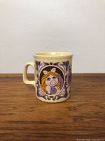 Front view of ceramic mug with Miss Piggy cartoon illustration and purple decorative elements
