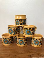 Front view of five vintage floral mugs stacked with one sugar bowl on top, showing the flower design and colors