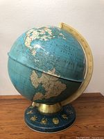 Full view of the vintage globe on its horoscope decorated base showing the Atlantic Ocean and portions of North and South America.