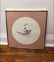 Frontal photo of the framed white cat print on the floor against a wall, showcasing the entire frame and artwork.