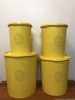 Front view of all four yellow Tupperware canisters stacked in two columns showing the vintage floral design on the front of each canister.