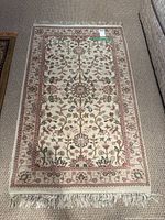Full view of the rectangular area rug showing cream background with pink and green floral patterns and fringed edges.