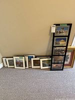 Several framed travel-themed pictures leaned against a wall including a tall black frame with five photos and multiple smaller frames