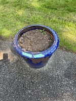 Blue garden pot outdoors on concrete and grass background, showing full pot and soil interior.