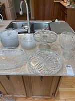 Overview of all glass items laid out on kitchen counter including small plates, large plates, bowl, and pedestal cake stand.