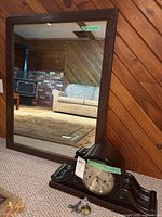 Dark wood framed rectangular mirror and dark wood mantle clock on floor with tools and size tags visible.
