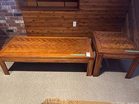 Photo showing both wooden tables side by side against wooden paneled and brick walls. Coffee table is long and rectangular, side table is square and smaller.