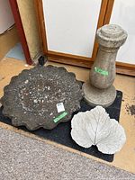 Overall view of three concrete items: birdbath bowl with pedestal base and leaf decor on black mat