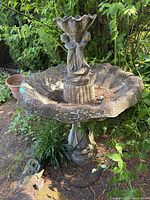 Full view of two-tiered concrete fountain in outdoor setting with surrounding plants.