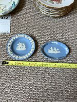 Two small Wedgwood blue jasperware trinket dishes on carpet with measuring tape showing about 3 to 4 inches diameter