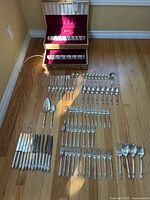 Full layout of all flatware pieces on floor with two open wooden canteens in background showing insert slots.