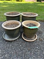 Four garden pots with soil, arranged on a driveway, showing the set and their heavy ceramic-like material.