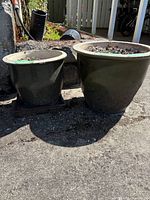 Two outdoor green garden pots side by side on concrete surface in sunlight, showing overall size and condition.