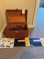 Open wooden box showing metal Meccano parts inside along with three instruction booklets in front of the box