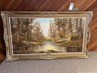 Full frontal view of painting showing landscape scene with forest and river in ornate gold frame
