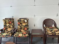 Four brown plastic patio chairs with floral cushions set against a white garage door, showing two adjustable recliner chairs on the left and two stationary chairs on the right, along with two matching square side tables in the middle.