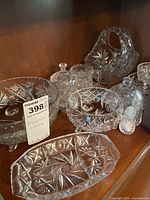 Assortment of Pinwheel Crystal items arranged on wood shelf showing various bowls, a covered butter dish, relish dish, glass basket with handle, and salt and pepper shakers.