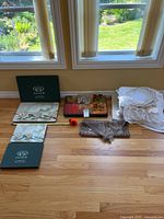 Full view of all included items: placemats boxed sets, napkin rings in a box, white linens folded, carved wooden decorative piece on floor.