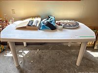 White plastic rectangular outdoor table with white legs, viewed from above showing badminton and croquet equipment and dartboard placed on it.