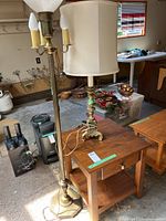 Wooden side table with drawer and two lamps, floor lamp with three bulbs and glass shade, ornate table lamp with fabric shade.